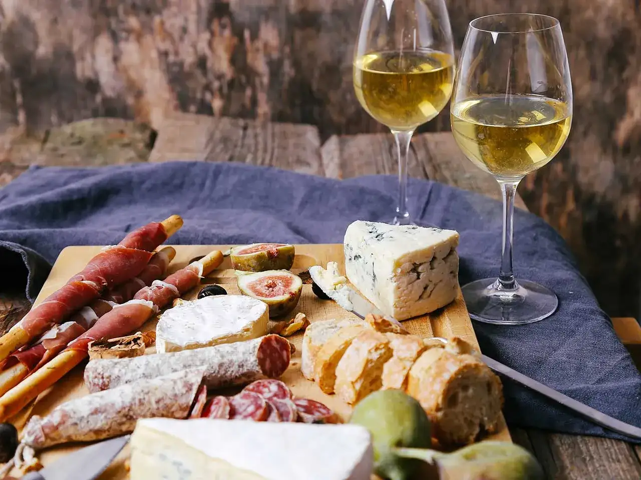 Un tagliere ricco di salumi, formaggi, fichi e pane, accompagnato da due calici di vino bianco. Un'invitante degustazione di vino e formaggio.