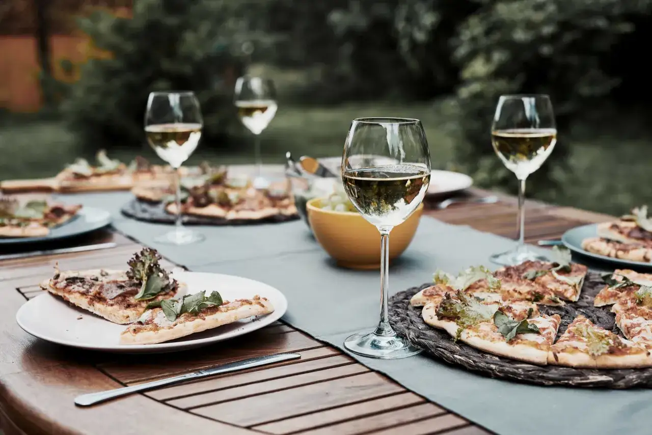 Tavola apparecchiata all'aperto con pizze e bicchieri di vino bianco, perfetta per una cena con la pizza vino bianco o rosso.