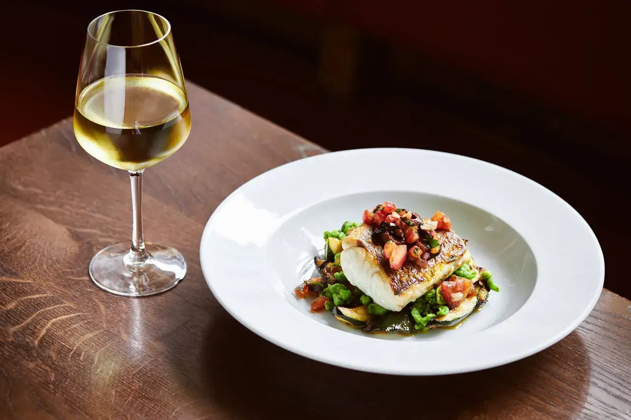 Piatto di pesce con verdure e un bicchiere di vino bianco, perfetti pinot grigio abbinamenti.