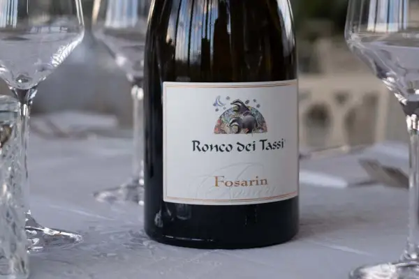 Bottiglia di vino Fosarin Ronco dei Tassi, tra calici pronti per degustare i vini del Collio.