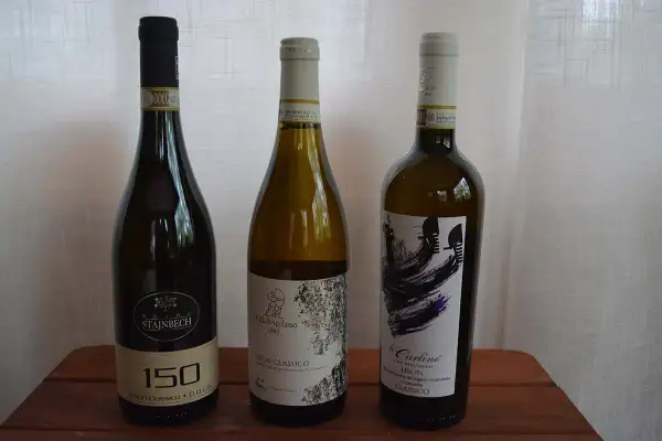 Tre bottiglie di vino bianco, tra cui un Lison Classico di Pramaggiore, su un tavolo di legno.