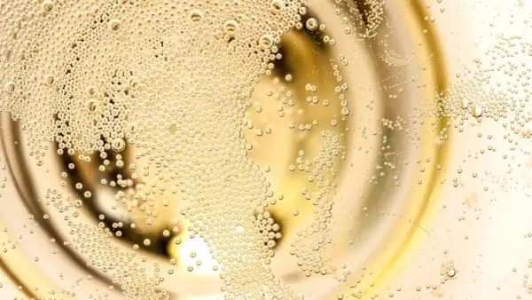 Bollicine dorate salgono in un bicchiere, evocando la freschezza di un Franciacorta Prosecco.
