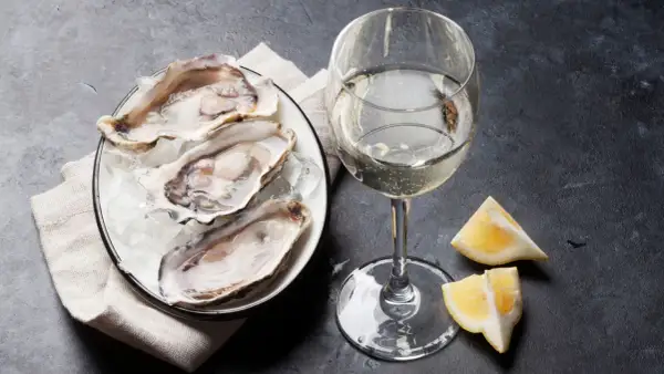 Piatto di ostriche fresche su ghiaccio, accompagnato da un bicchiere di vino francese per ostriche e spicchi di limone.