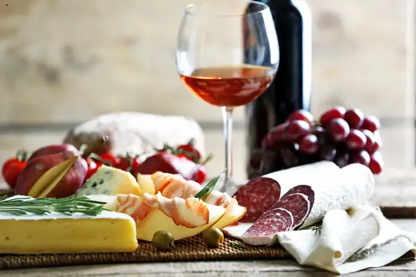 Tagliere con salumi, formaggi, uva e pane. Un bicchiere di vino rosato suggerisce perfetti vermentino abbinamenti.