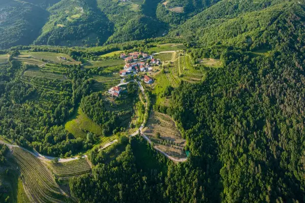 Un borgo pittoresco nel **Collio Goriziano**, immerso tra vigneti terrazzati e boschi lussureggianti, con case dai tetti rossi che si aggrappano alle dolci colline.