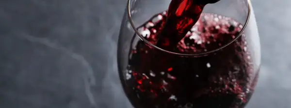 Versando vino rosso rubino in un calice, evocando i sapori autentici dei vini lucani.