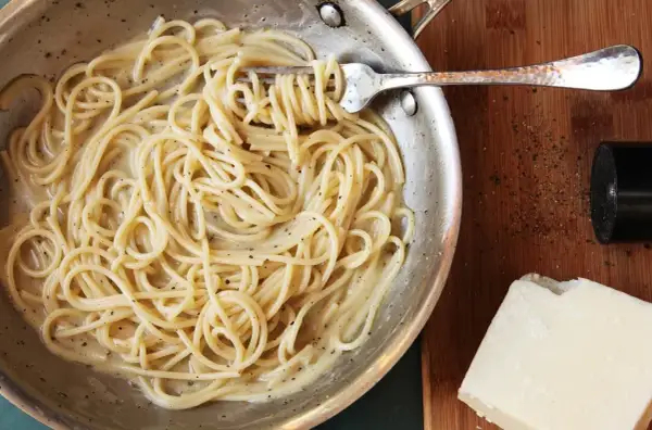 Spaghetti cacio e pepe cremosi, pronti per un perfetto abbinamento vino. Pepe macinato fresco e pecorino a lato.