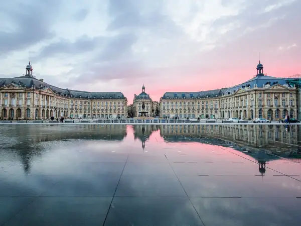 Piazza specchiata al tramonto, con edifici eleganti che ricordano il fascino del Medoc Bordeaux.