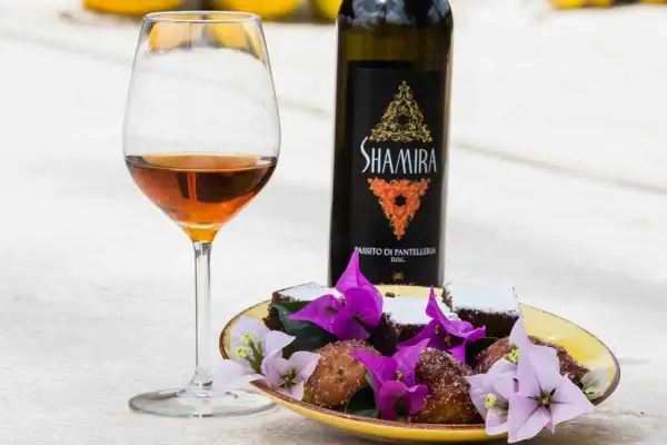 Calice di passito di Pantelleria accanto a dolcetti e fiori viola.