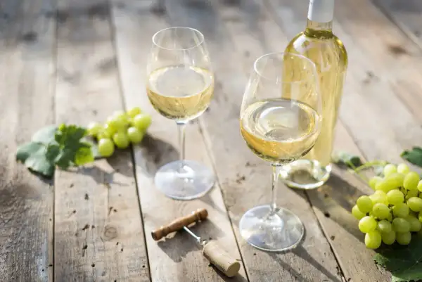 Due calici di vino bianco, una bottiglia, uva e cavatappi su un tavolo di legno. Le caratteristiche del Pouilly-Fumé si riflettono in questo scenario.