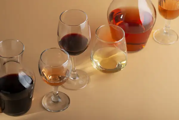 Bicchieri e caraffe con vino rosso, bianco e rosato. Un bicchiere di vino rosso, forse un Merlot, risalta tra gli altri.