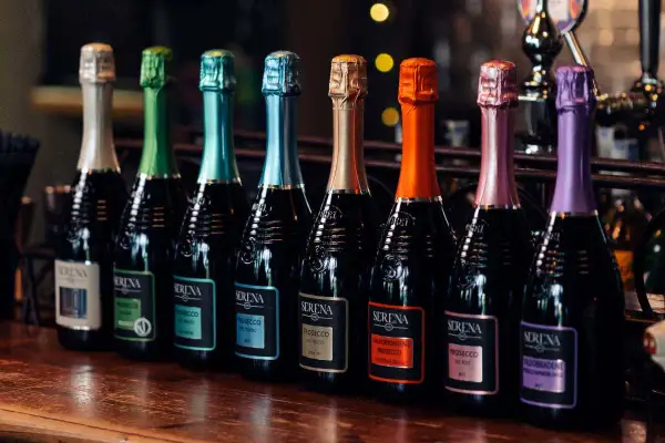 Una fila di bottiglie di Prosecco Serena, ognuna con un tappo colorato. Il brut è un Prosecco, perfetto per ogni occasione.