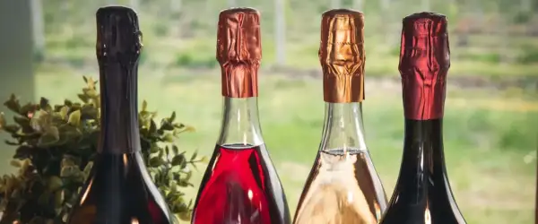 Quattro bottiglie di vini più pregiati, con tappi color rame, oro e rosso, pronte per essere degustate.