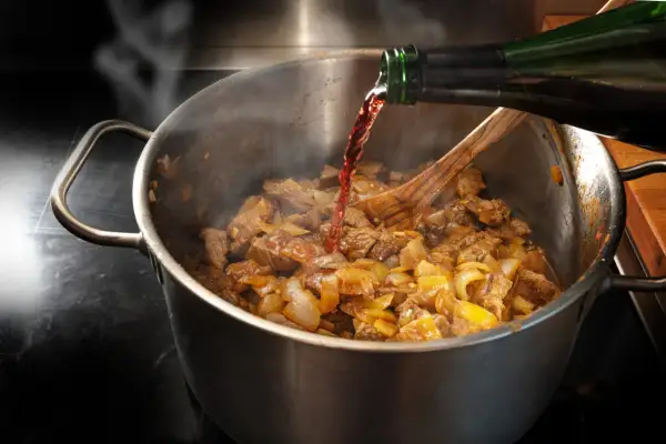 Carne e cipolle in cottura in una pentola, con vino rosso versato da una bottiglia. Un classico per le ricette con il vino rosso.