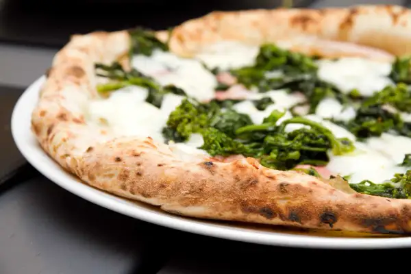 Pizza con verdure e mozzarella su un piatto bianco, un'ottima scelta per una serata con pizza e champagne.
