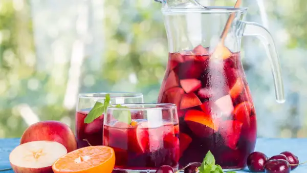 Caraffa e bicchieri pieni di sangria, con frutta fresca come mele, arance e ciliegie. Perfetta per fare la sangria in una giornata estiva.