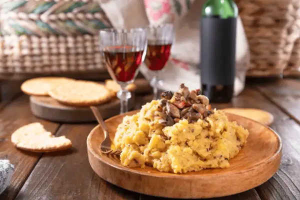 Polenta con funghi, perfetta con un buon vino da abbinare alla polenta. Due calici rossi e una bottiglia completano la scena rustica.