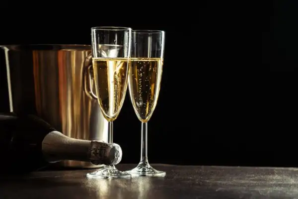 Due calici di champagne scintillante, una bottiglia e un secchiello per il ghiaccio. Un'uva per lo champagne, pronta per essere gustata.